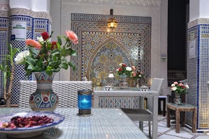 A room with a patterned tile wall, a table with a vase of flowers, and a chair.