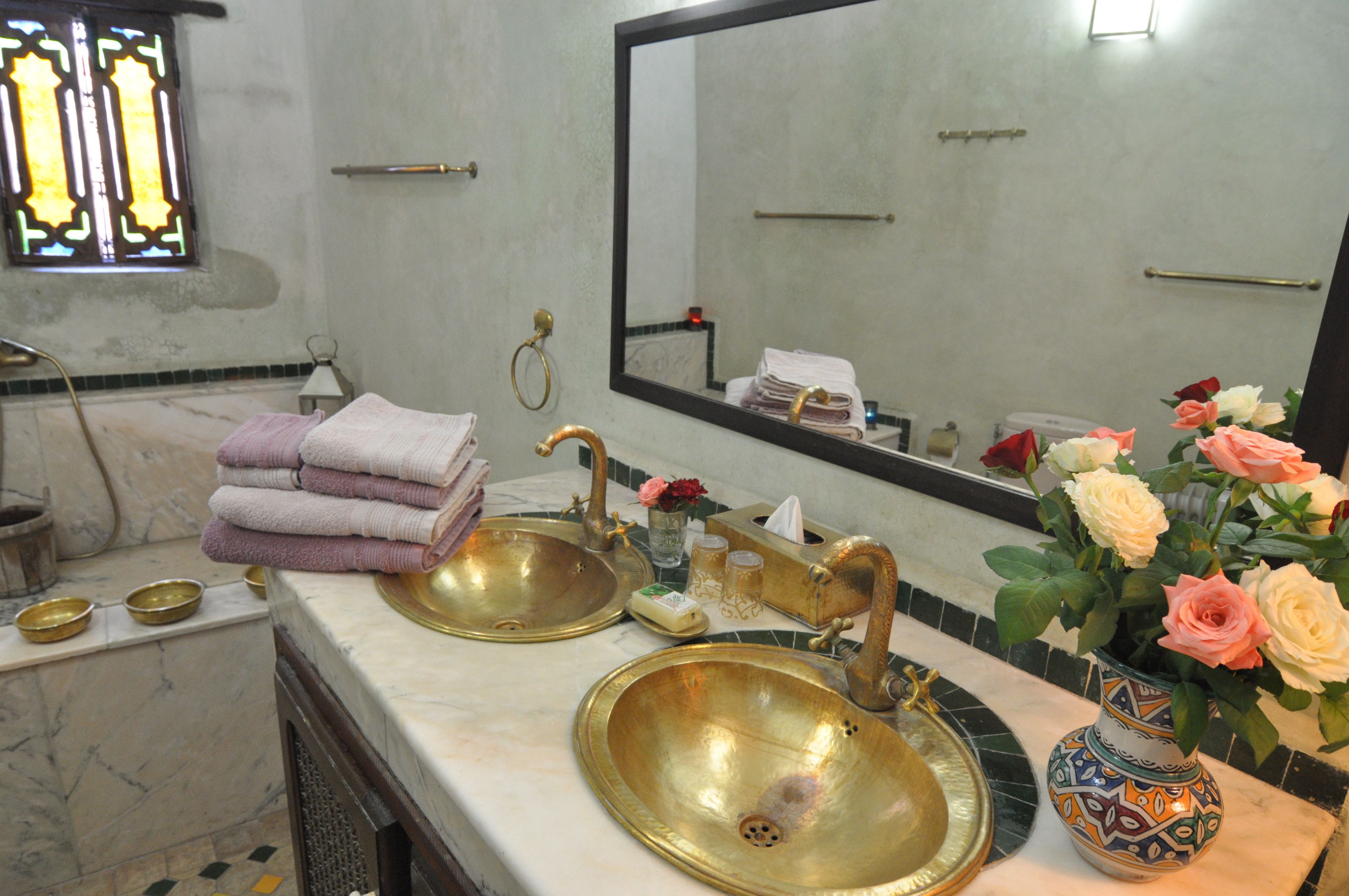 A bathroom with two sinks, a mirror, a window with stained glass, and a vase with flowers.