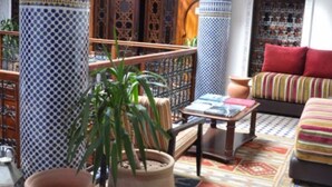 A cozy lounge area with a patterned floor, a sofa with colorful cushions, and a small table with books. - Riad Adarissa (Fes)