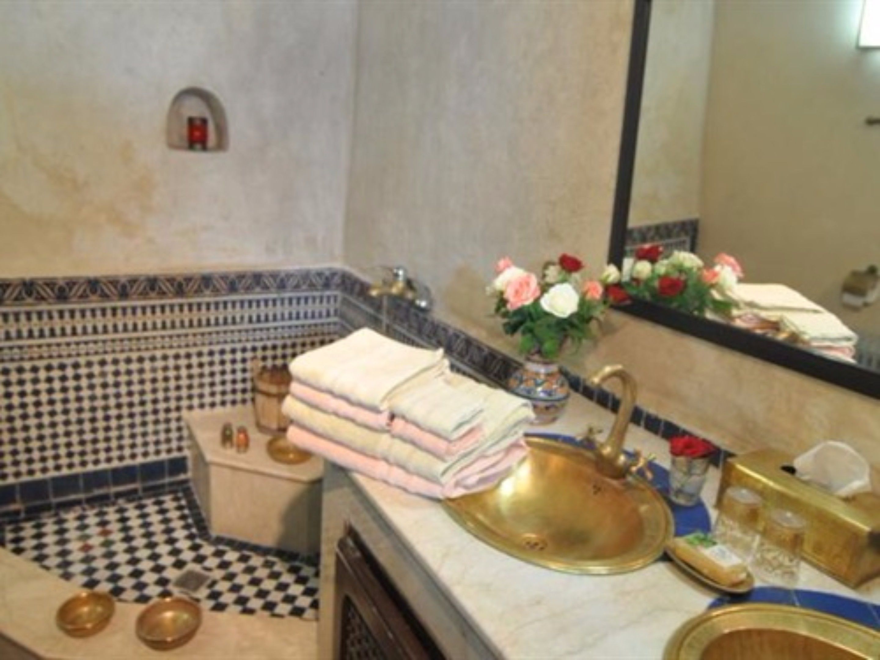A bathroom with a checkered floor, a sink with a gold basin, and a mirror reflecting a vase with flowers.
