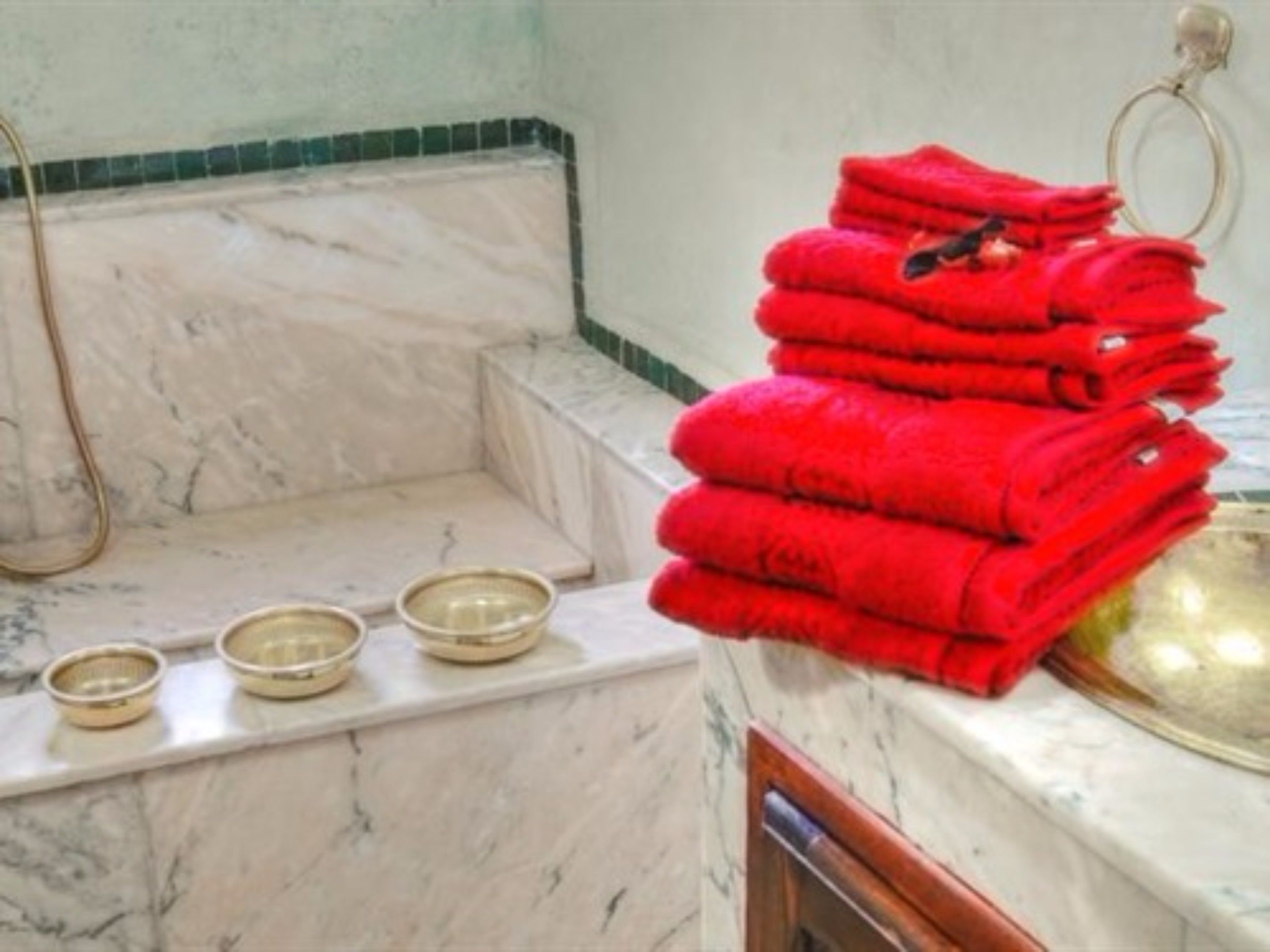 A bathroom with a marble sink, a stack of red towels, and three bowls on the counter.