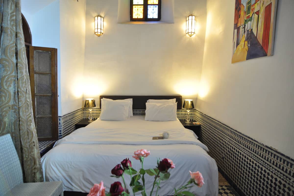 Habitación de hotel con una cama grande, dos mesitas de noche con lámparas, una ventana con vistas y un cuadro en la pared.
