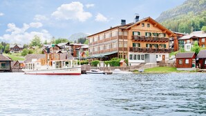 A wooden building with balconies, a boat docked in front, and a mountainous backdrop.