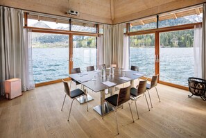 A conference room with a table, chairs, and a projector. It has large windows with curtains, a wooden floor, and a view of a lake and mountains. - TAUROA Seehotel Grundlsee (Grundlsee)