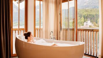 A woman relaxing in a large bathtub with a view of a castle through the windows.