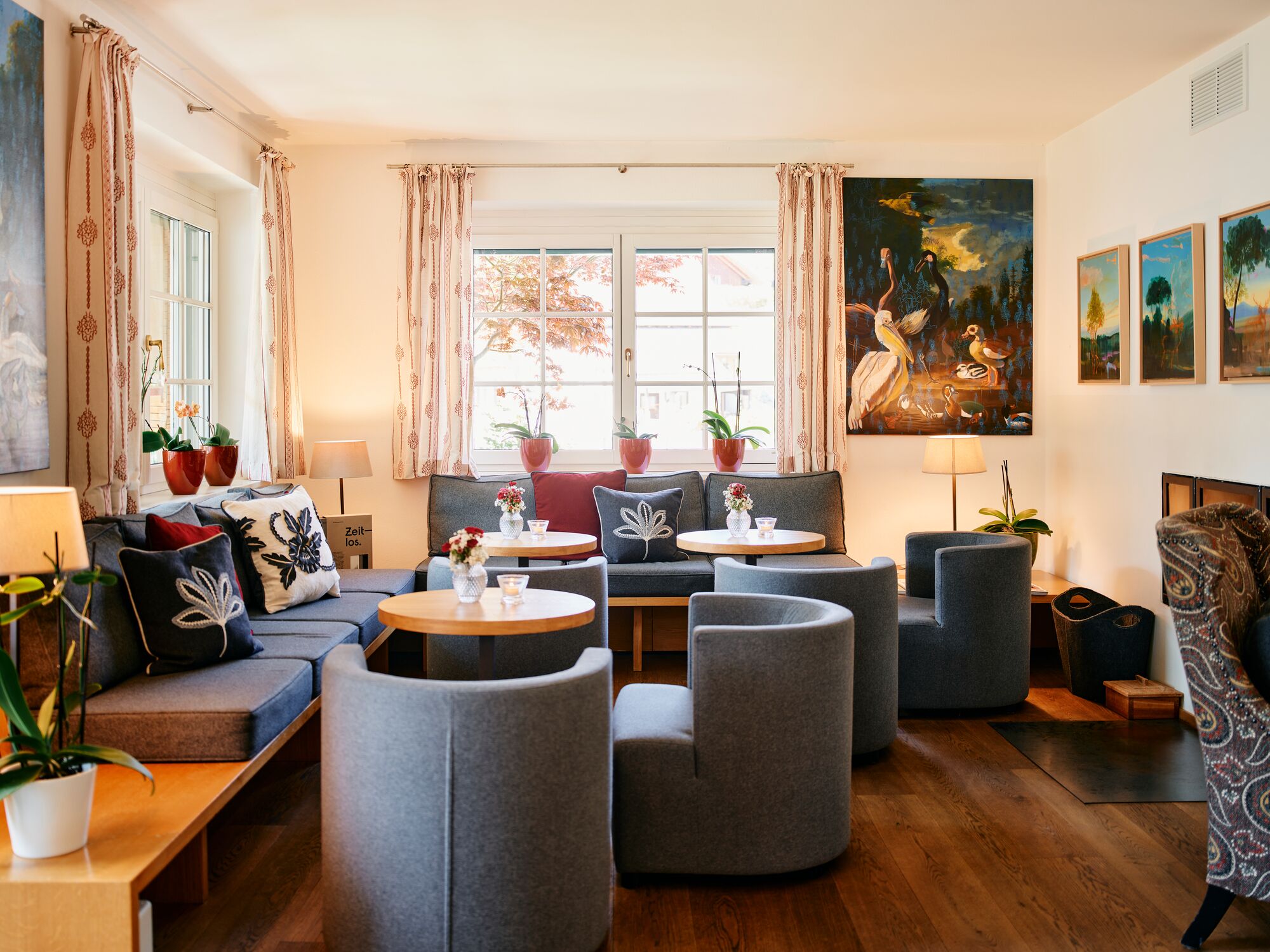 A modern lounge area with sofas, armchairs, and a coffee table, featuring artwork and potted plants.