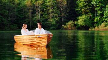 A wooden boat on a calm lake surrounded by dense green forest.