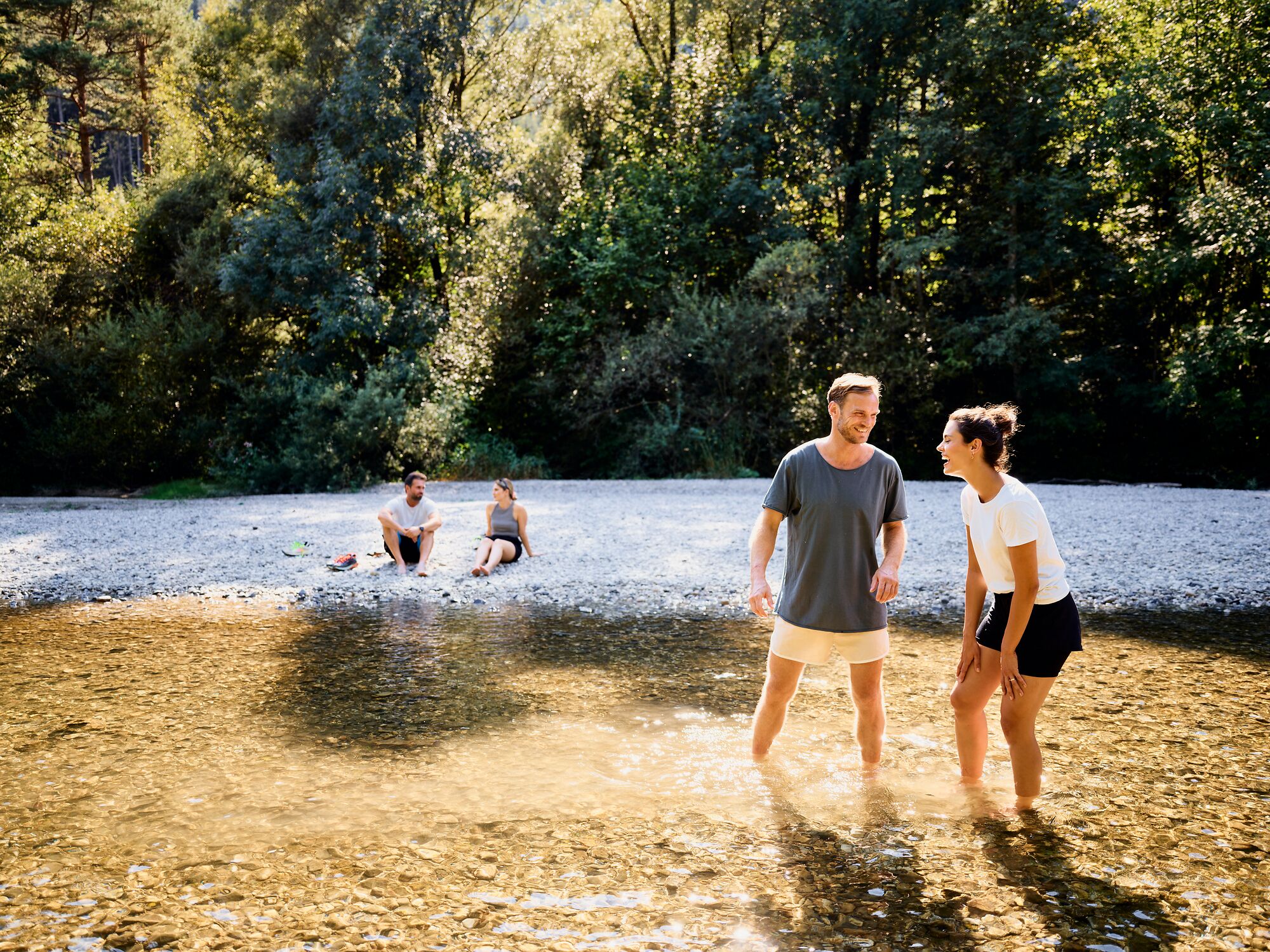 A riverbank with people sitting and standing in the water.