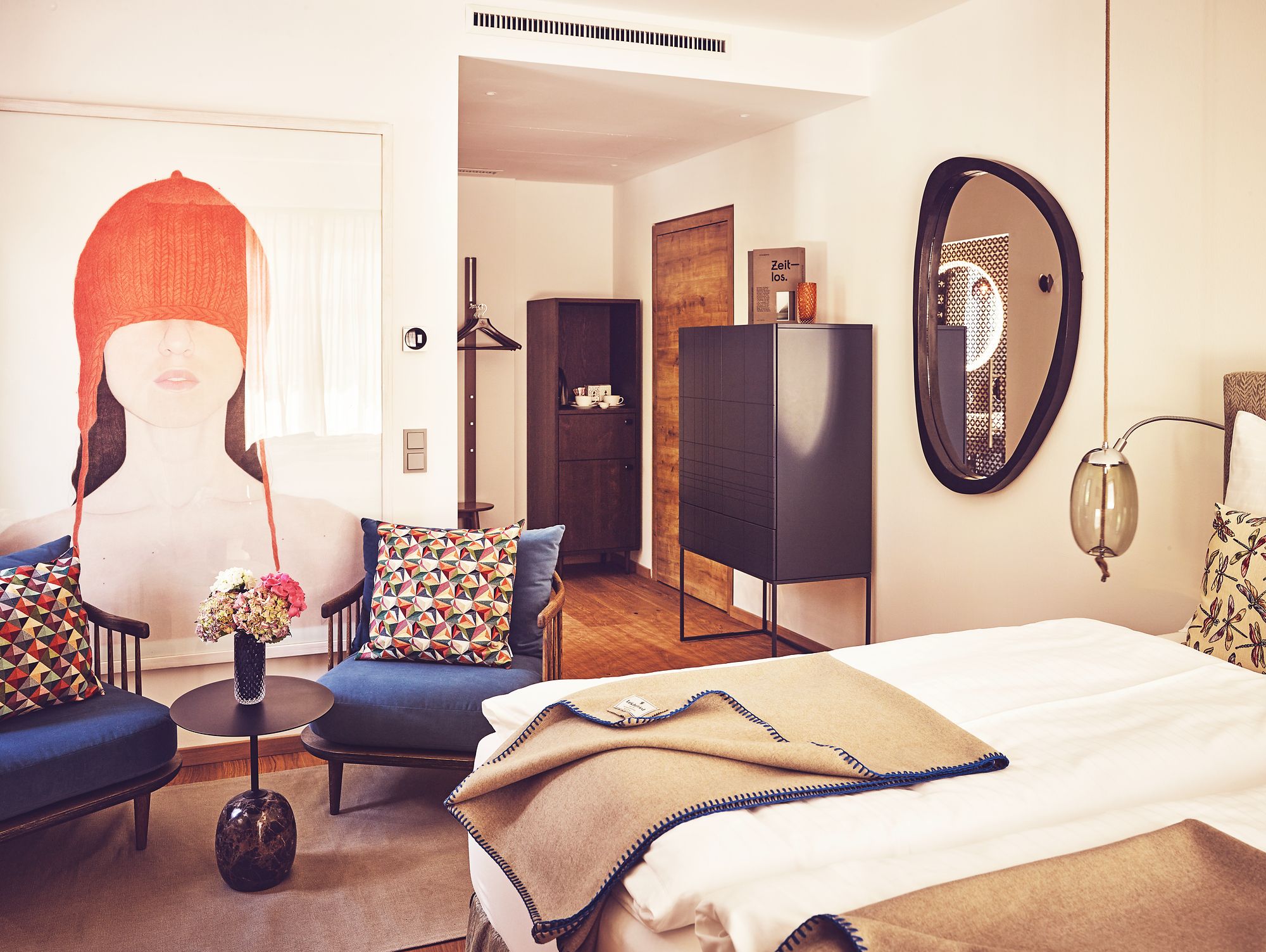 Une chambre d’hôtel moderne équipée d’un lit, d’un canapé, d’une chaise, d’une petite table et d’un miroir.
