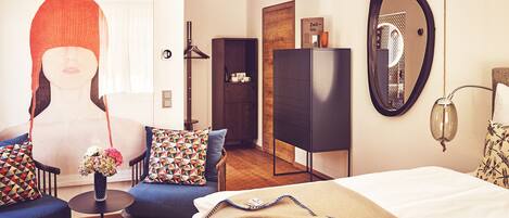 Une chambre d’hôtel moderne équipée d’un lit, d’un canapé, d’une chaise, d’une petite table et d’un miroir.