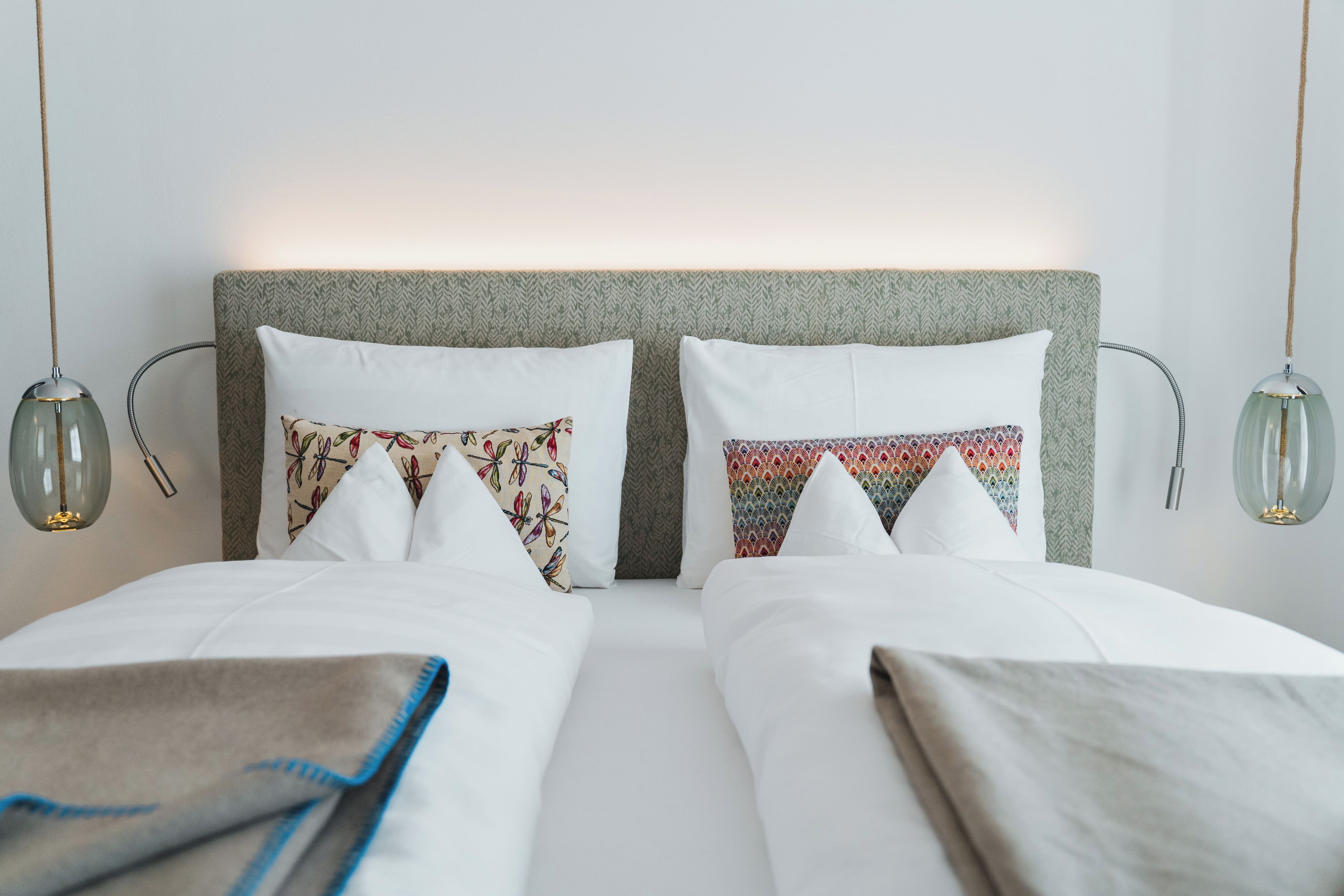 Ein Doppelbett mit weißen Bettlaken und zwei Kissen, eines mit Blumenmuster und das andere mit geometrischem Design.