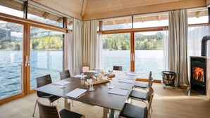Un interior de madera con una gran mesa y sillas, chimenea y vistas a un lago.