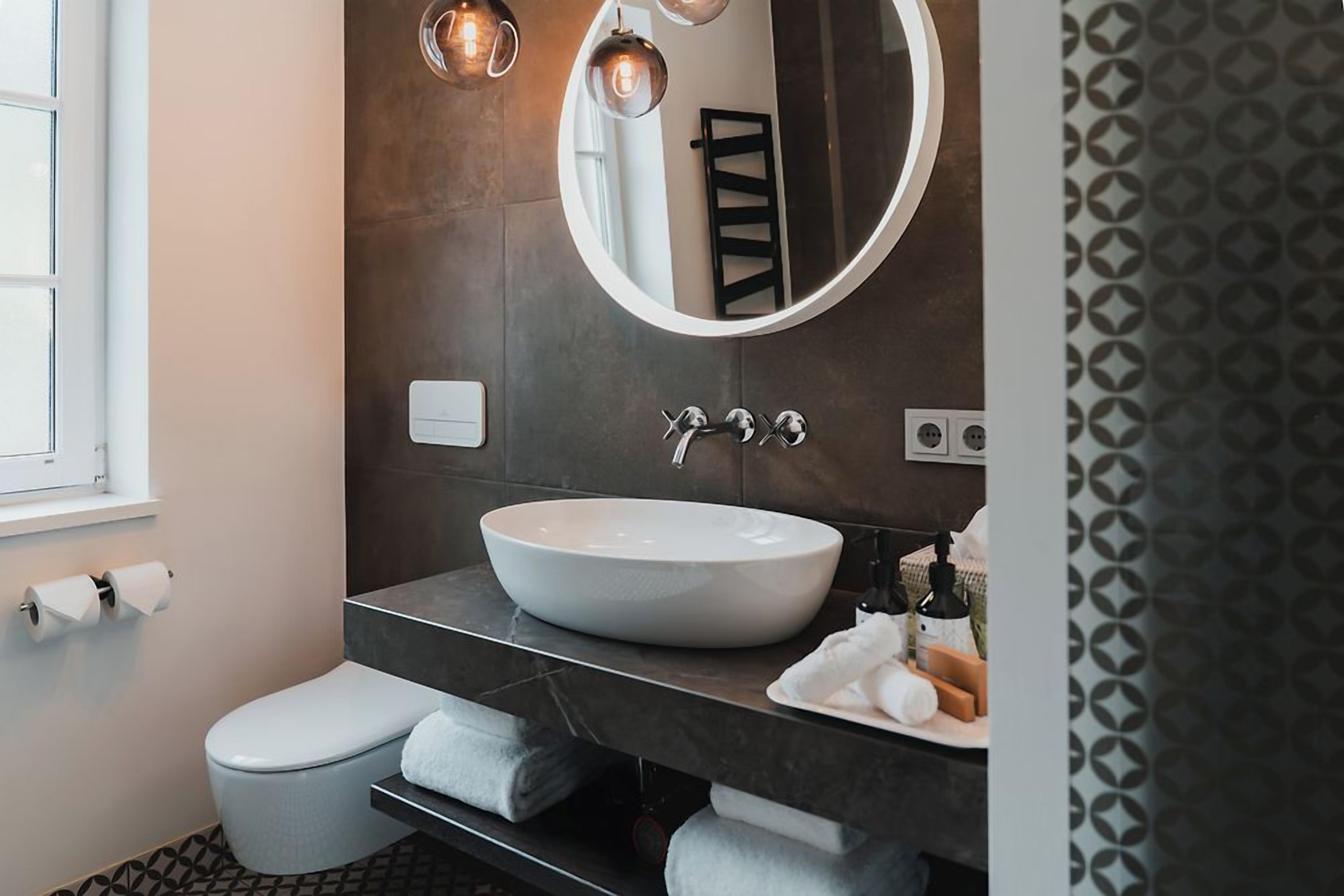 Ein modernes Badezimmer mit einem runden Spiegel, einem Aufsatzwaschbecken und einer Toilette.