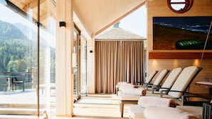 Una habitación iluminada por el sol con vistas a una montaña boscosa, una piscina y una mesa con un juego de mesa verde.