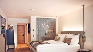 A modern hotel room with a large bed, a bedside table, a lamp, and a decorative wall panel. - TAUROA Seehotel Grundlsee (Grundlsee)