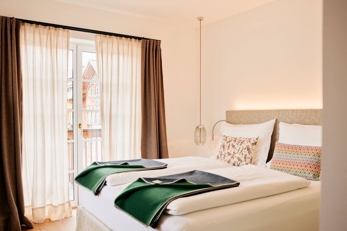 Ein Hotelzimmer mit Bett, Blick durch das Fenster und einer Pendelleuchte.