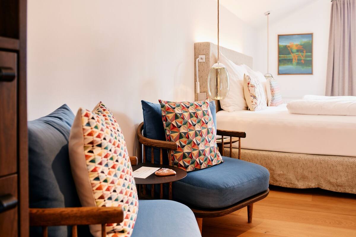 Ein Hotelzimmer mit einem Bett, zwei blauen Sesseln und einem Holztischchen.