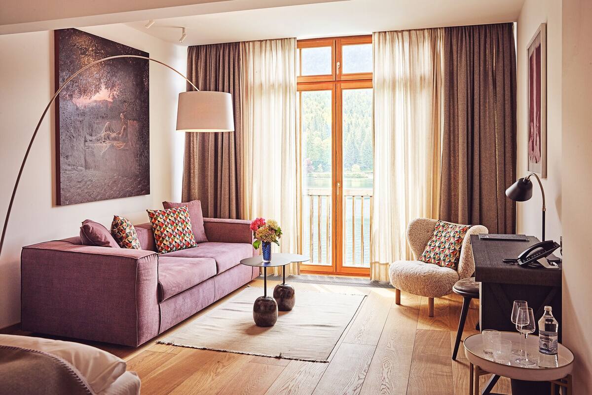 Ein modernes Wohnzimmer mit einer Couch, einem Sessel und einem kleinen Tisch mit Gläsern und einer Flasche.