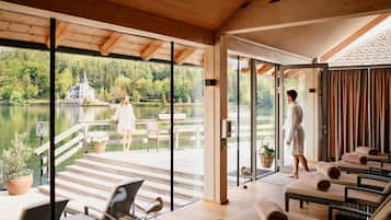 Un spa moderno con una gran puerta de vidrio que da a una terraza con vistas a un lago, amueblado con sillas y una mesa.