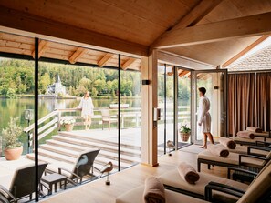 A modern spa room with a large glass door leading to a deck overlooking a lake, furnished with chairs and a table. - TAUROA Seehotel Grundlsee (Grundlsee)