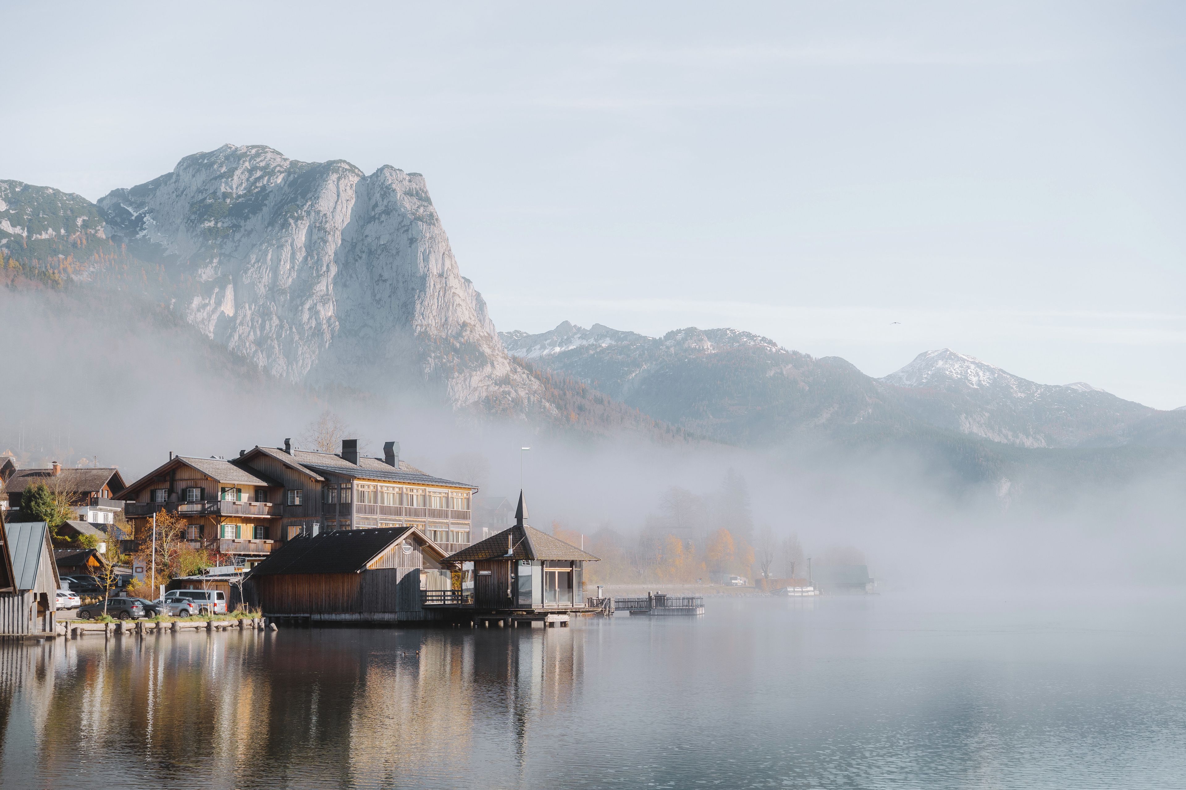 A lakeside village with traditional wooden buildings, a dock, and mountains in the background.