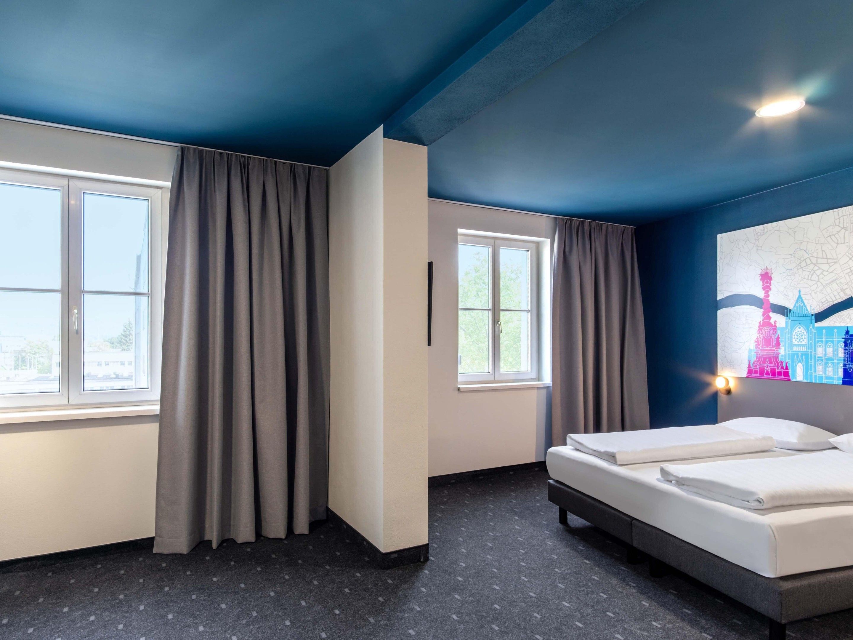 Habitación de hotel con una cama, dos ventanas y una obra de arte colgada en la pared.