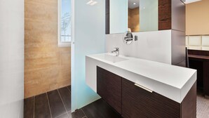 Ein modernes Badezimmer mit weißem Waschtisch, dunklen Holzschränken, einem großen Spiegel und einem Fenster mit Jalousien.