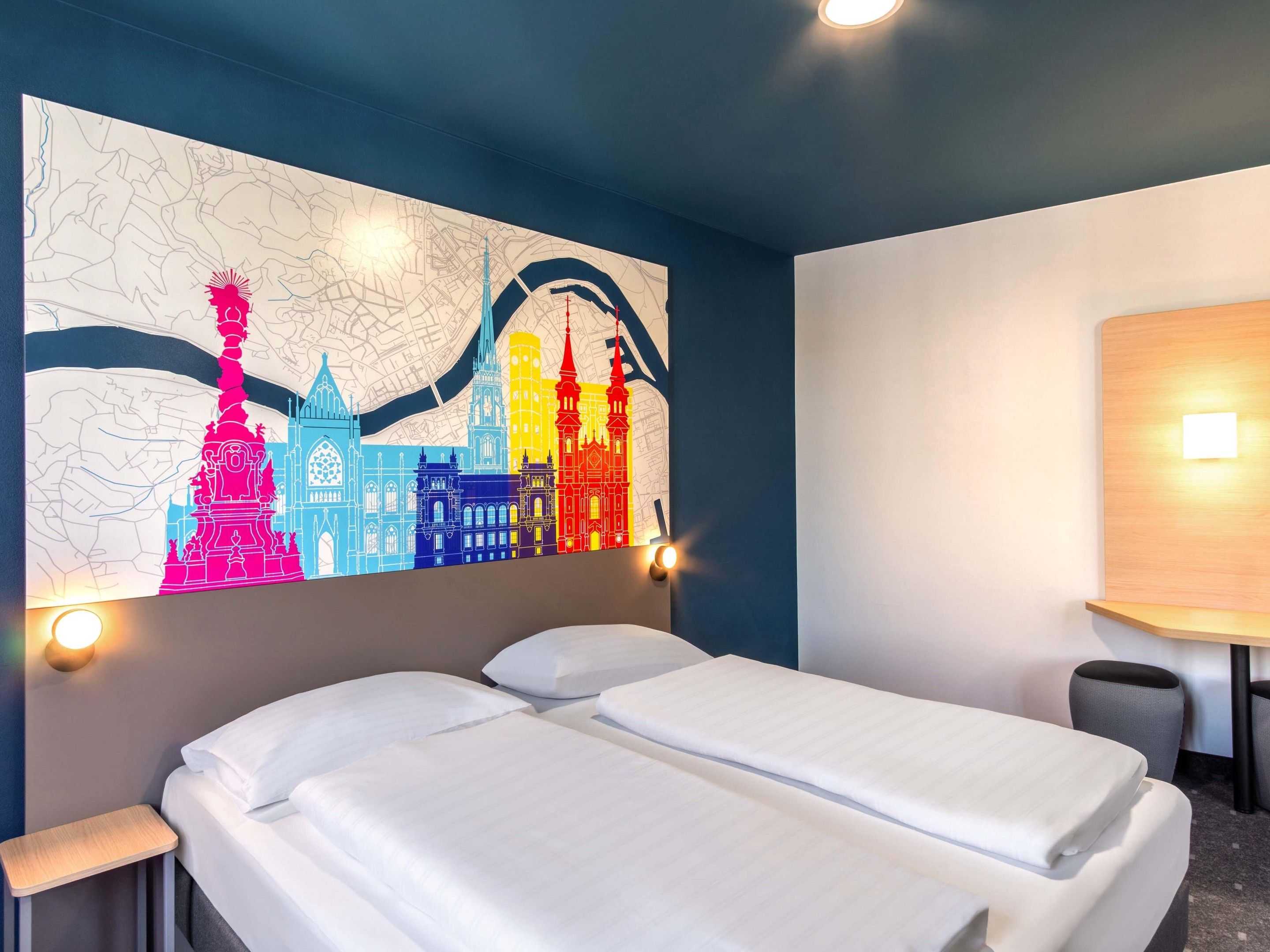 Habitació d'hotel amb dos llits, un mapa penjat a la paret i una taula petita amb una cadira.