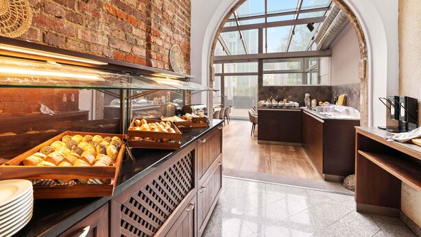 Ein Frühstücksbuffet mit Gebäck, eine Ziegelwand und Blick durch ein rundbogenförmiges Fenster.
