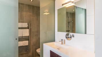 Un baño moderno con cabina de ducha de vidrio, un tocador blanco con espejo y un inodoro.