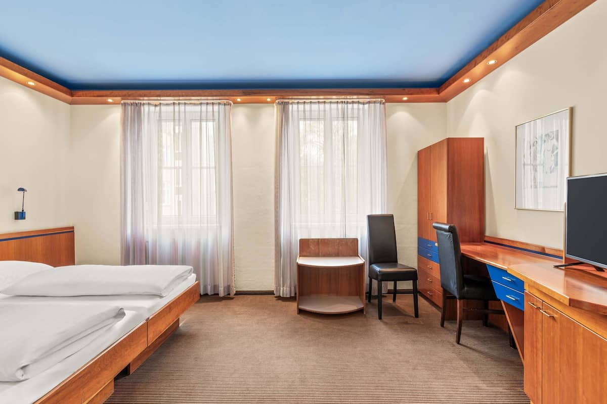 A hotel room with a bed, desk, chair, wardrobe, and a television.