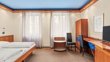 Una habitación de hotel con cama, escritorio, silla, armario y televisor.