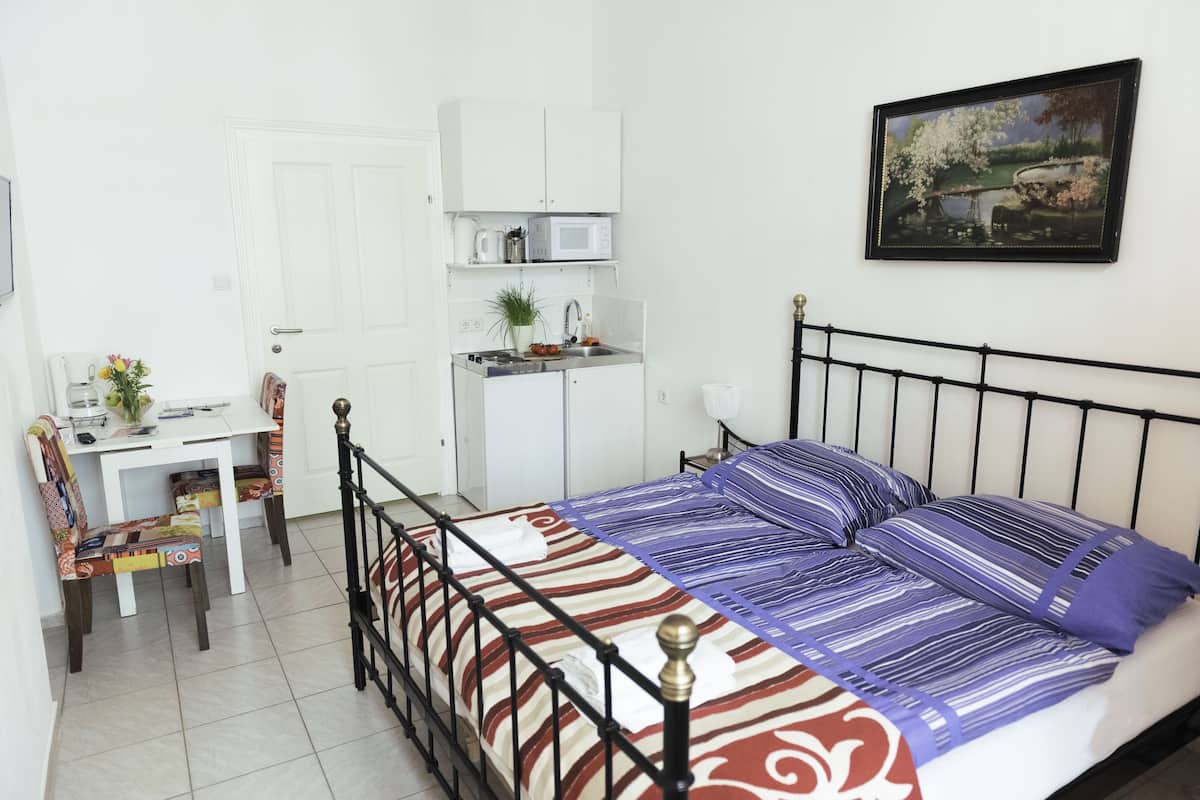 Un dormitorio con cama, escritorio, silla, una pequeña cocina americana y un cuadro en la pared.