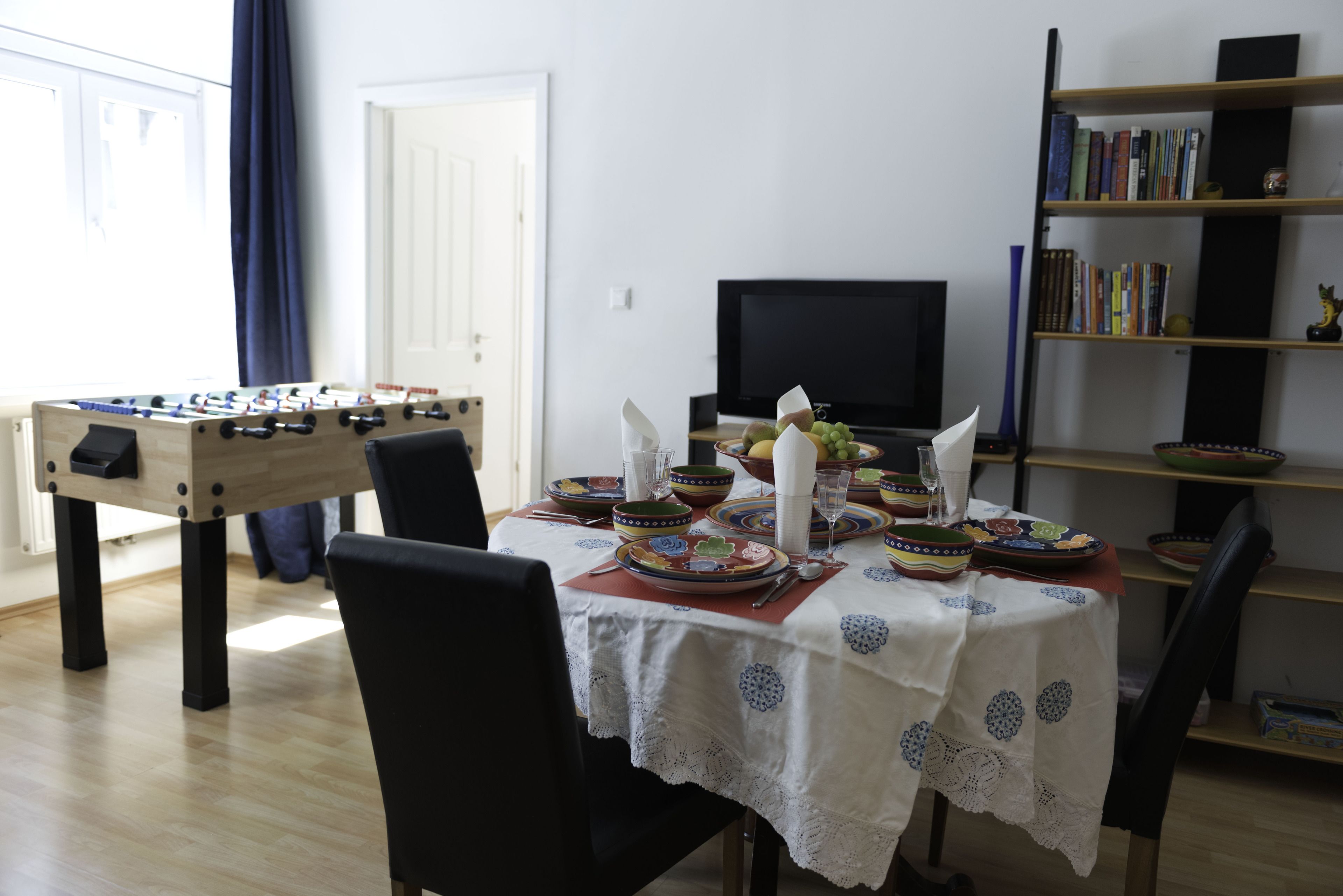 A dining area with a foosball table, a television, and a bookshelf.