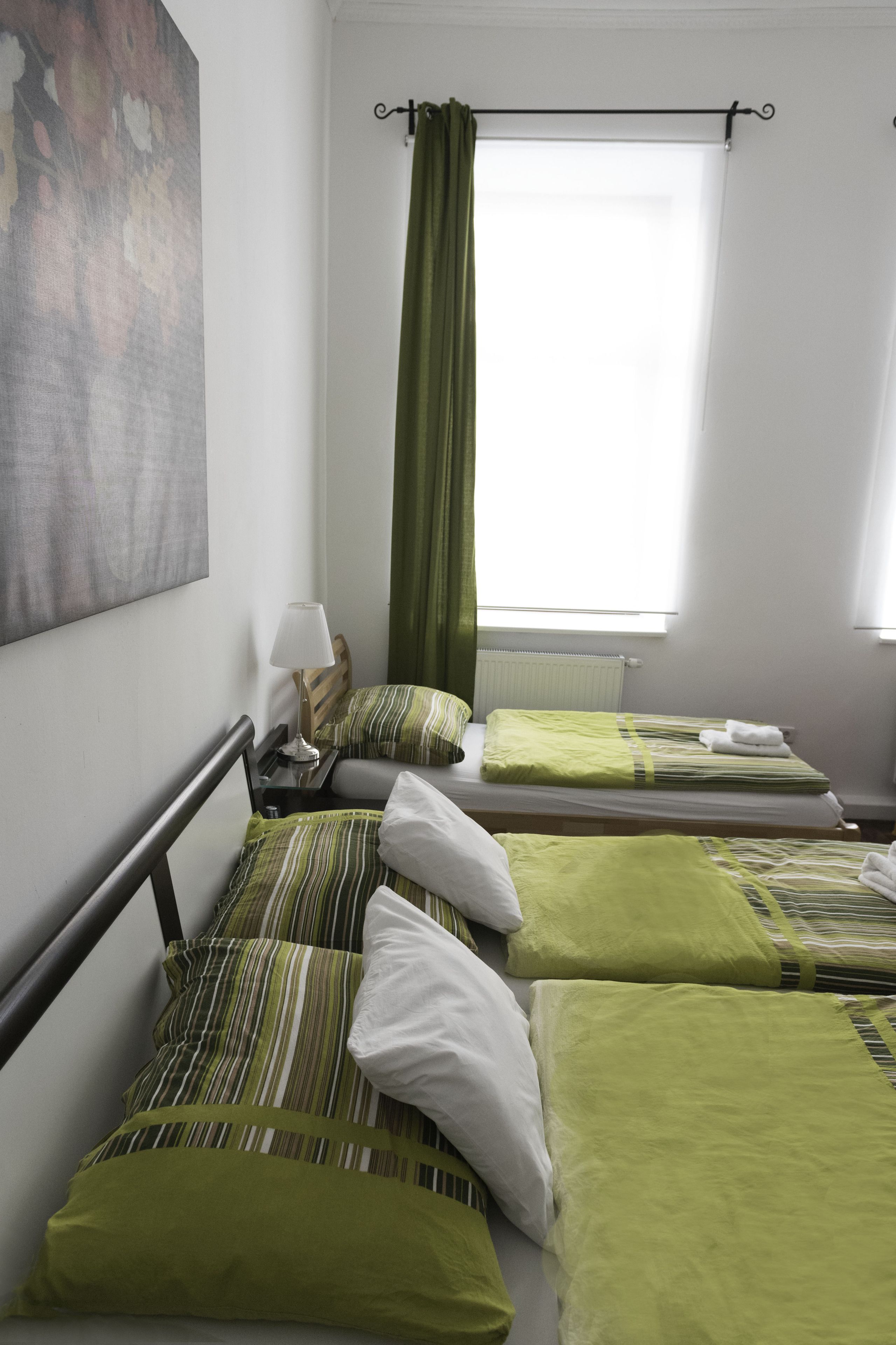 Habitación de hotel con dos camas individuales, cada una con ropa de cama verde y blanca a rayas, una mesita de noche con lámpara y un cuadro abstracto grande en la pared.