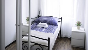 A bedroom with a bed, a nightstand, a chandelier, and a window with sheer curtains. - Old Vienna Apartments (Vienna)