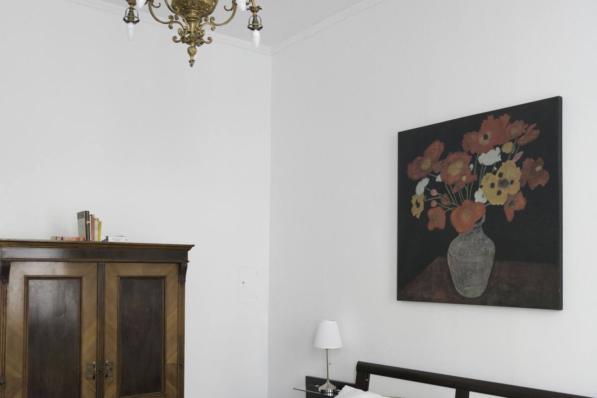 Un dormitorio con cama, armario de madera, candelabro, cuadro y mesita de noche.