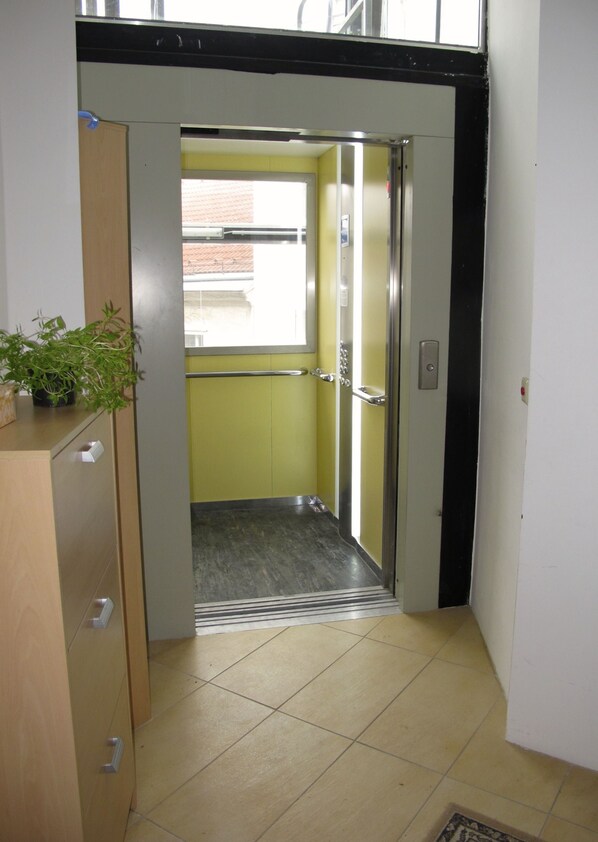 An elevator with a metal handrail, a potted plant on the left, and a tiled floor. - Old Vienna Apartments (Vienna)