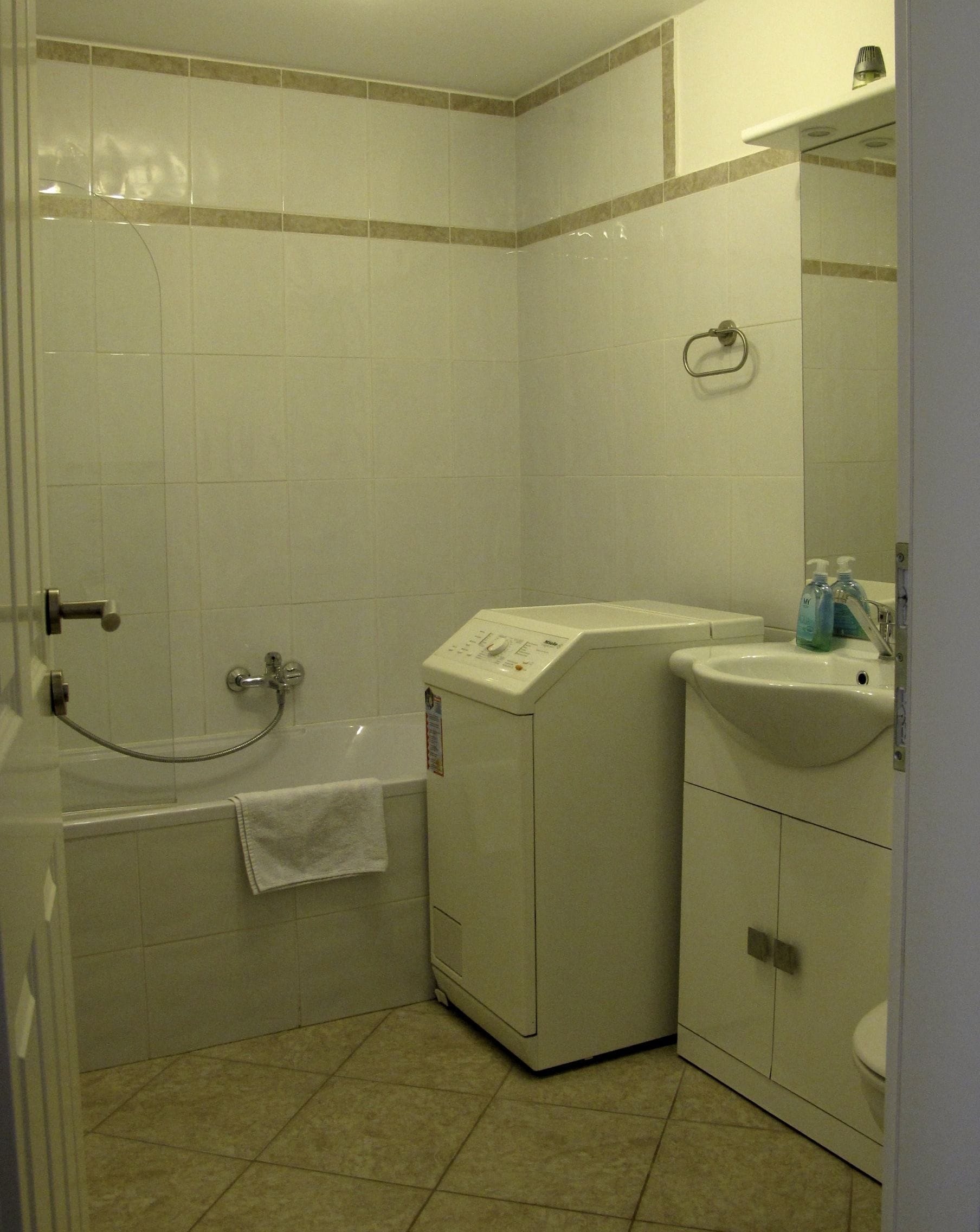 A small, clean bathroom with a shower, a sink, and a washing machine.