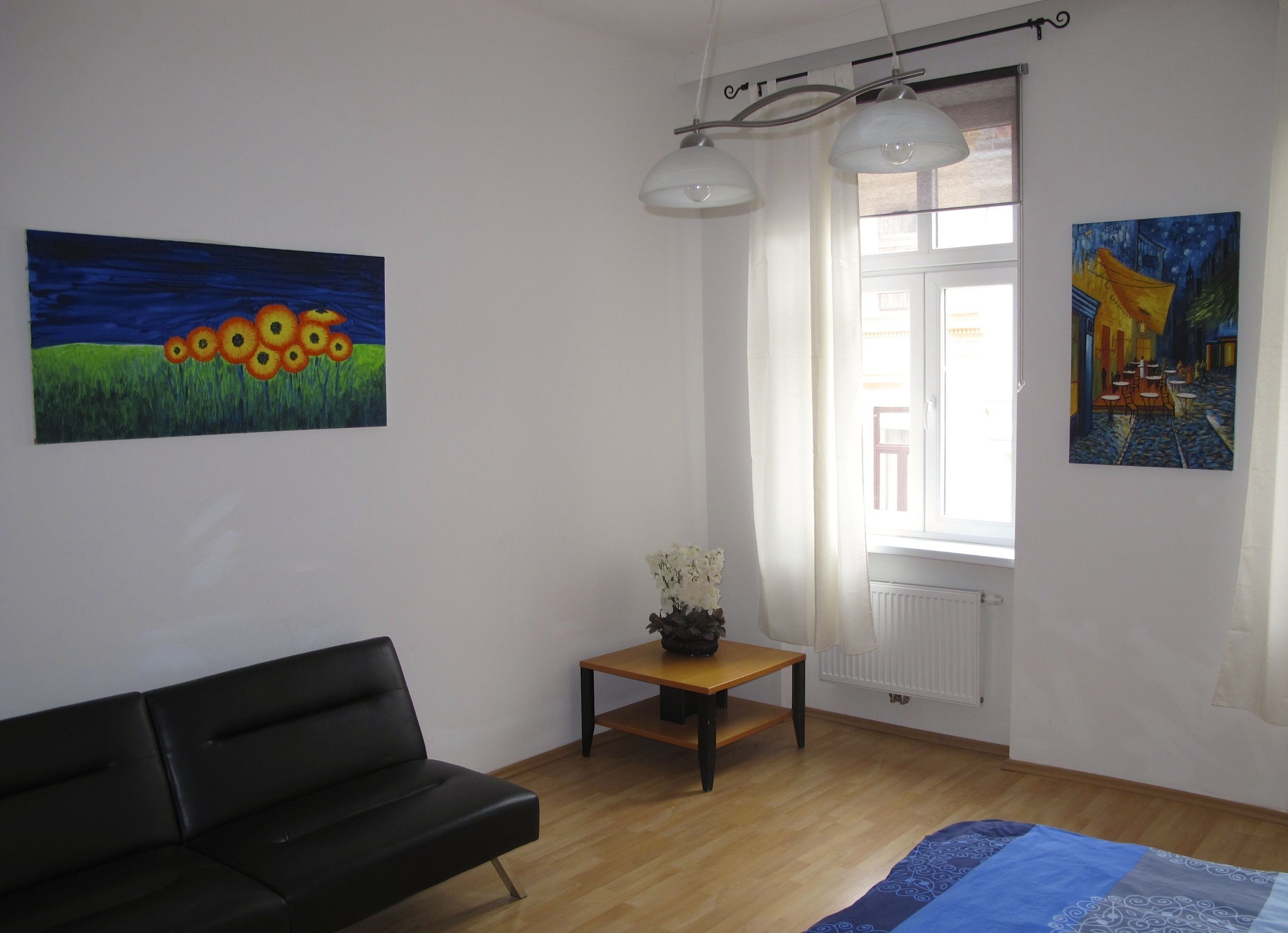Une pièce avec un canapé en cuir noir, une table en bois ornée d’un vase de fleurs et deux tableaux accrochés aux murs.
