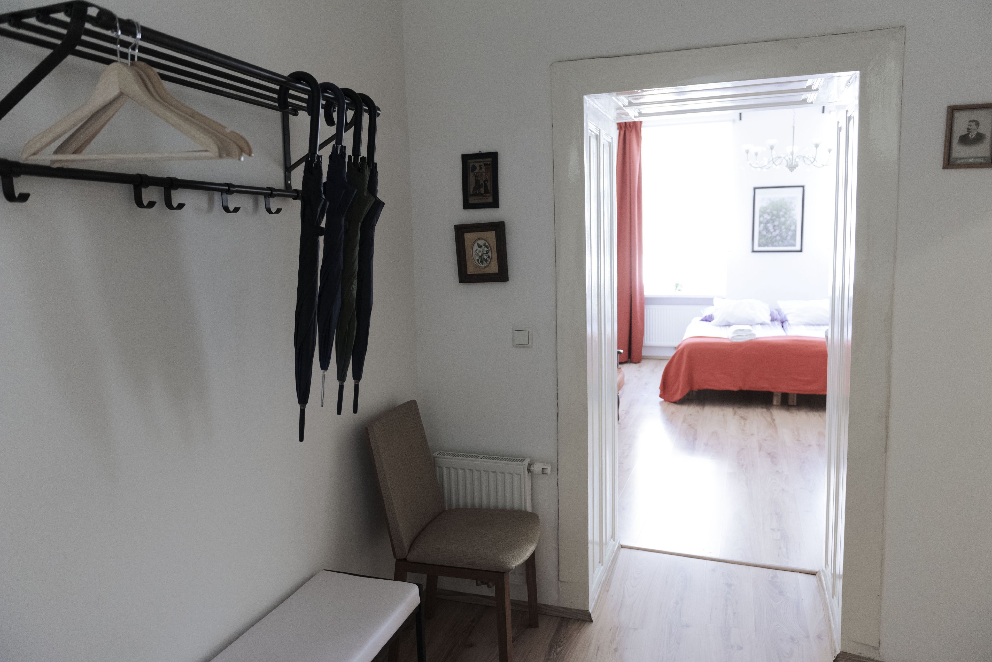 A bedroom with a bed, a chair, a radiator, and a coat rack with hangers.