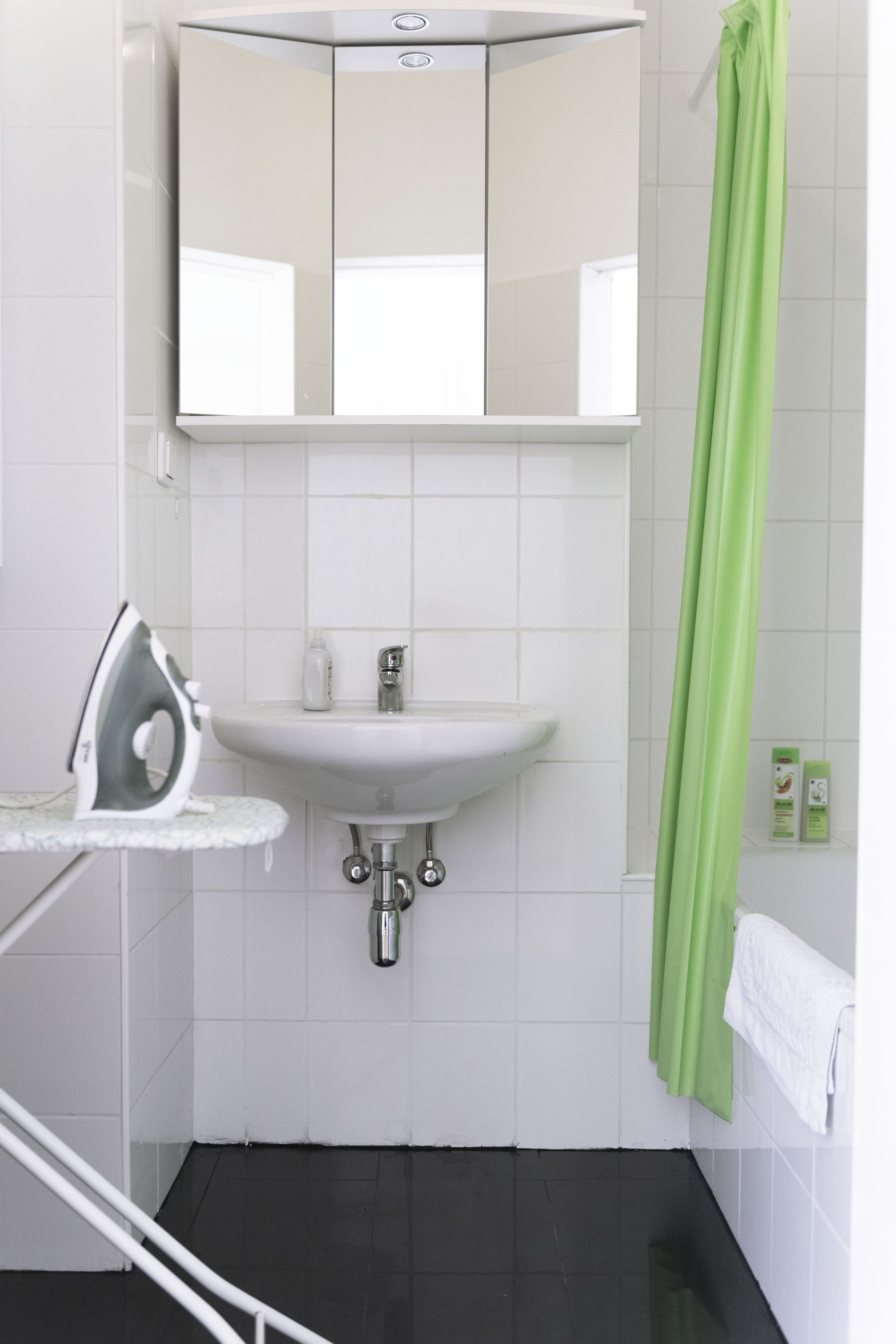 A bathroom with a white sink, a mirror above it, a green shower curtain, and a white towel hanging on the wall.
