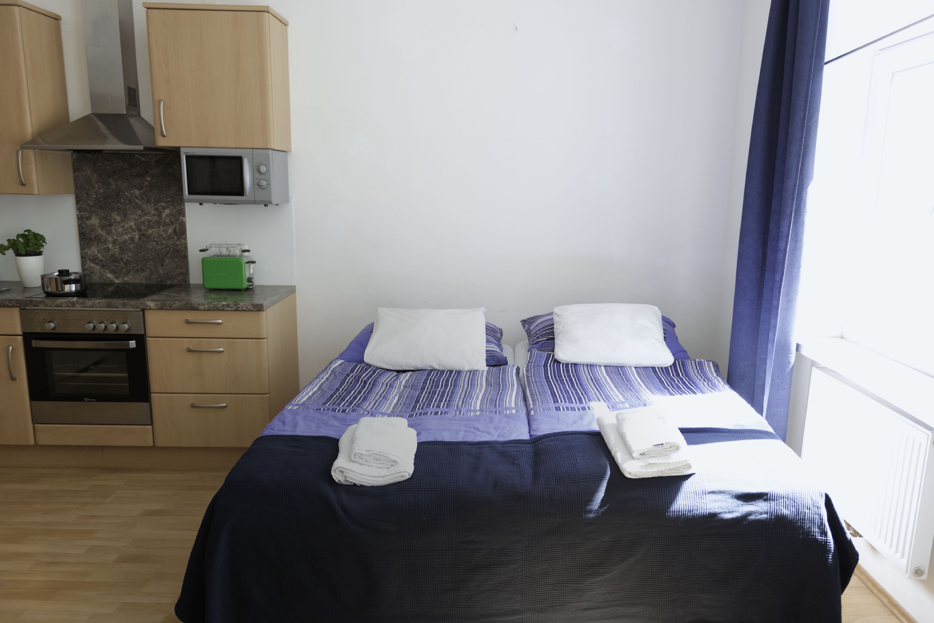 A small, clean room with a bed, a microwave, a toaster, and a small kitchen area.