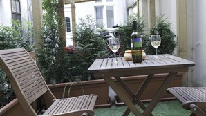 An outdoor patio with wooden furniture and a table set for two, featuring a bottle and glasses. - Old Vienna Apartments (Vienna)