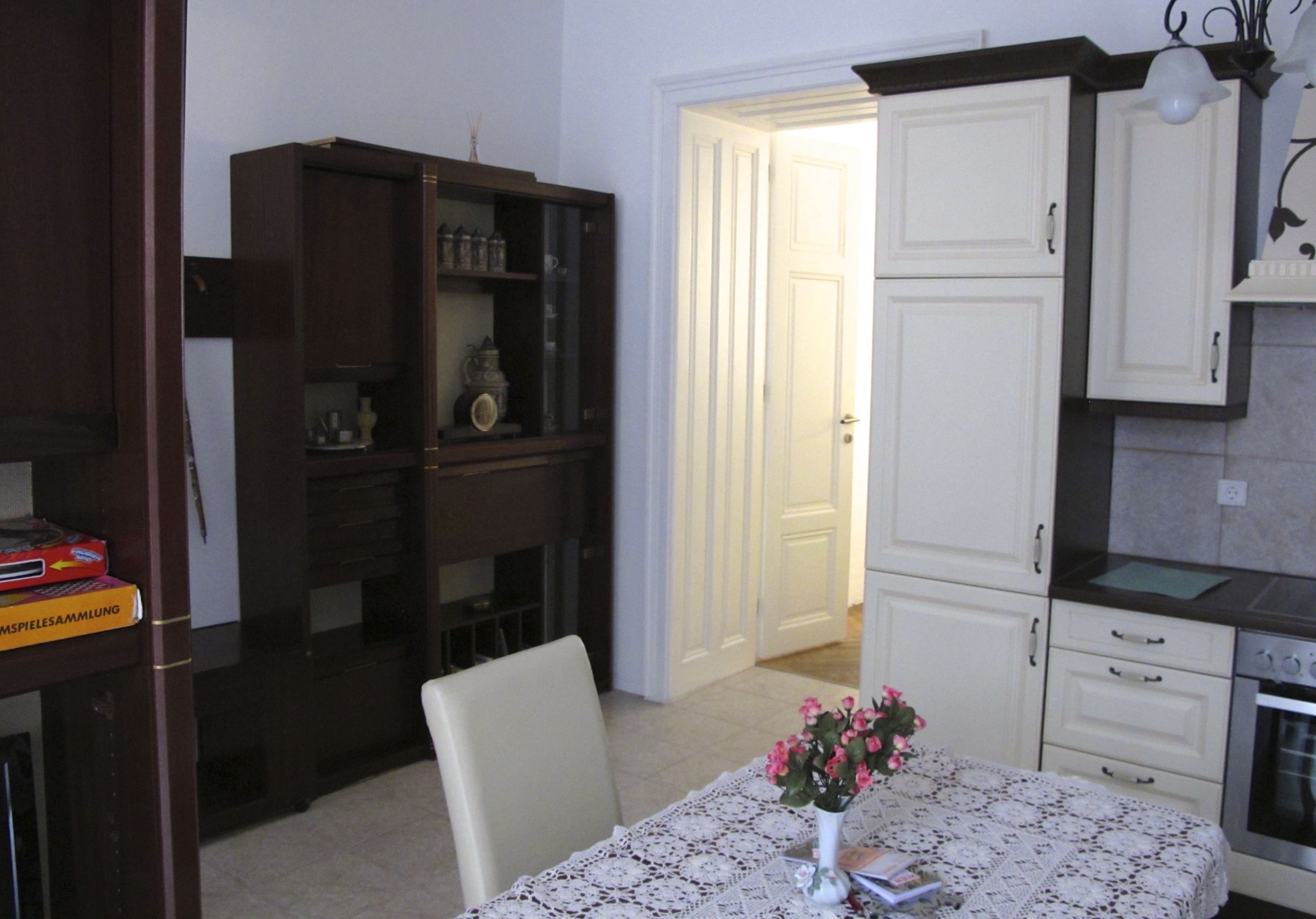 Un coin repas avec une table dressée pour deux personnes, un meuble avec des portes en verre et un espace cuisine équipé d’une cuisinière.