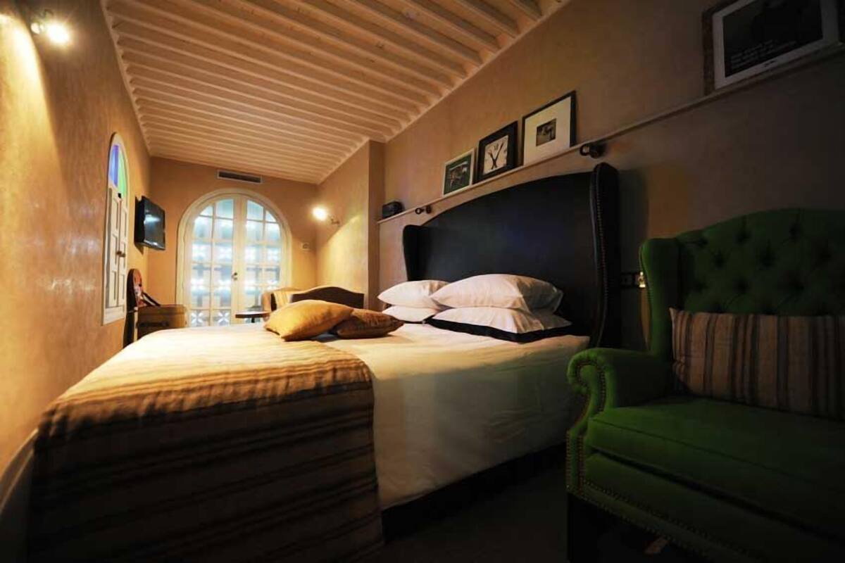 Un dormitorio con una cama grande, un sillón verde y una ventana con vistas.