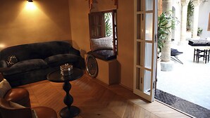 A cozy living room with a sofa, a coffee table, and a chair. There is a door leading to an outdoor area with plants and a patio.