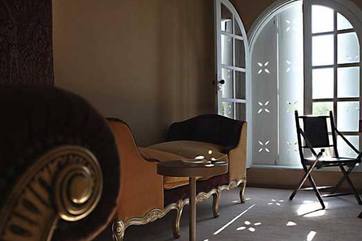 Una habitación con sofá, una silla, una mesa y un amplio ventanal que deja entrar luz natural.