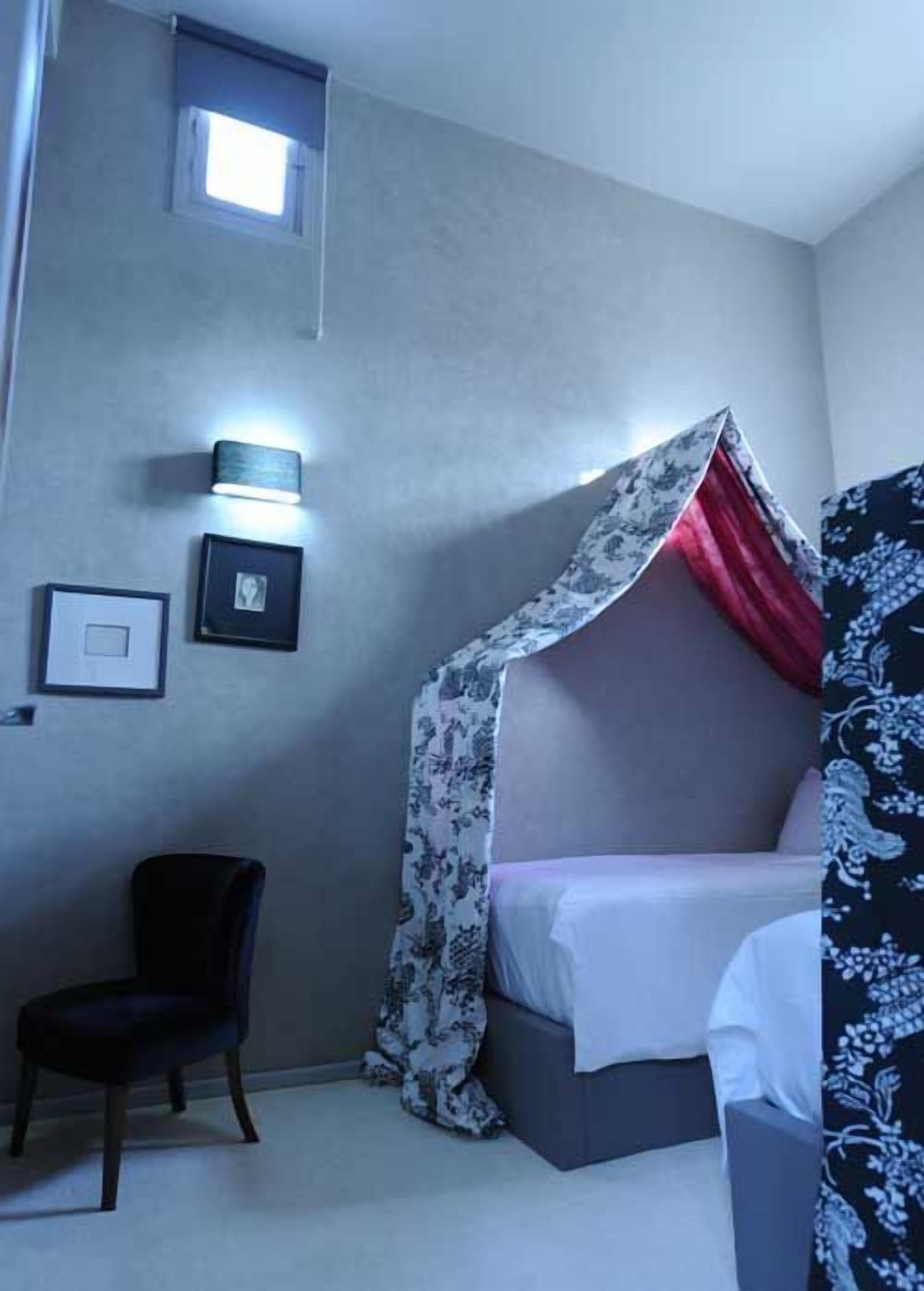 Una habitación con cama bajo un dosel, una silla y una lámpara fijada a la pared.