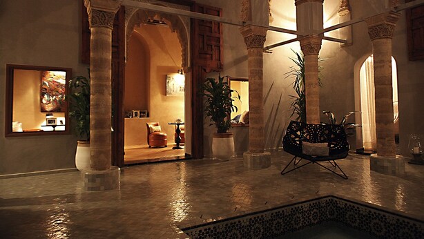 A spacious interior with high arches and columns, a seating area with a plant, and a view into a room with a fireplace.